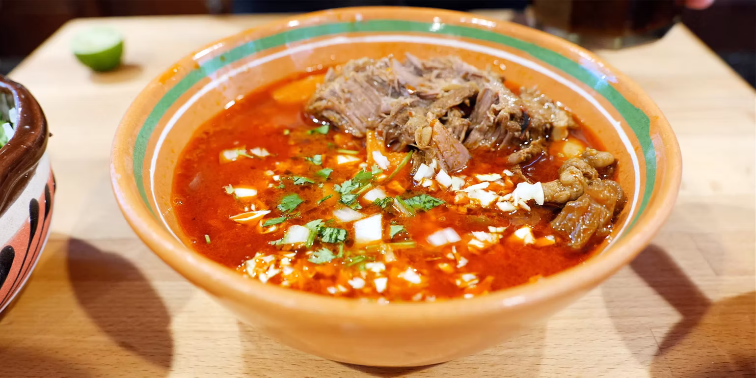 Rich birria in a traditional clay bowl with shredded beef, white onion and cilantro at Roberta's Cocina Mexicana