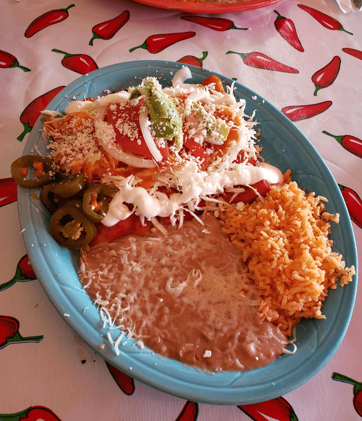 Enchiladas rojas with guacamole, Spanish rice and refried beans on a blue plate at Roberta's Cocina Mexicana